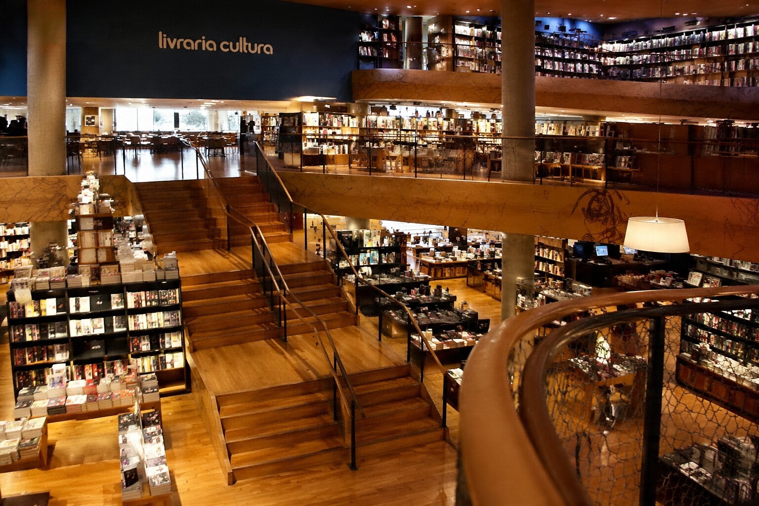 Interior de uma livraria charmosa com estantes de madeira, café e luz natural.